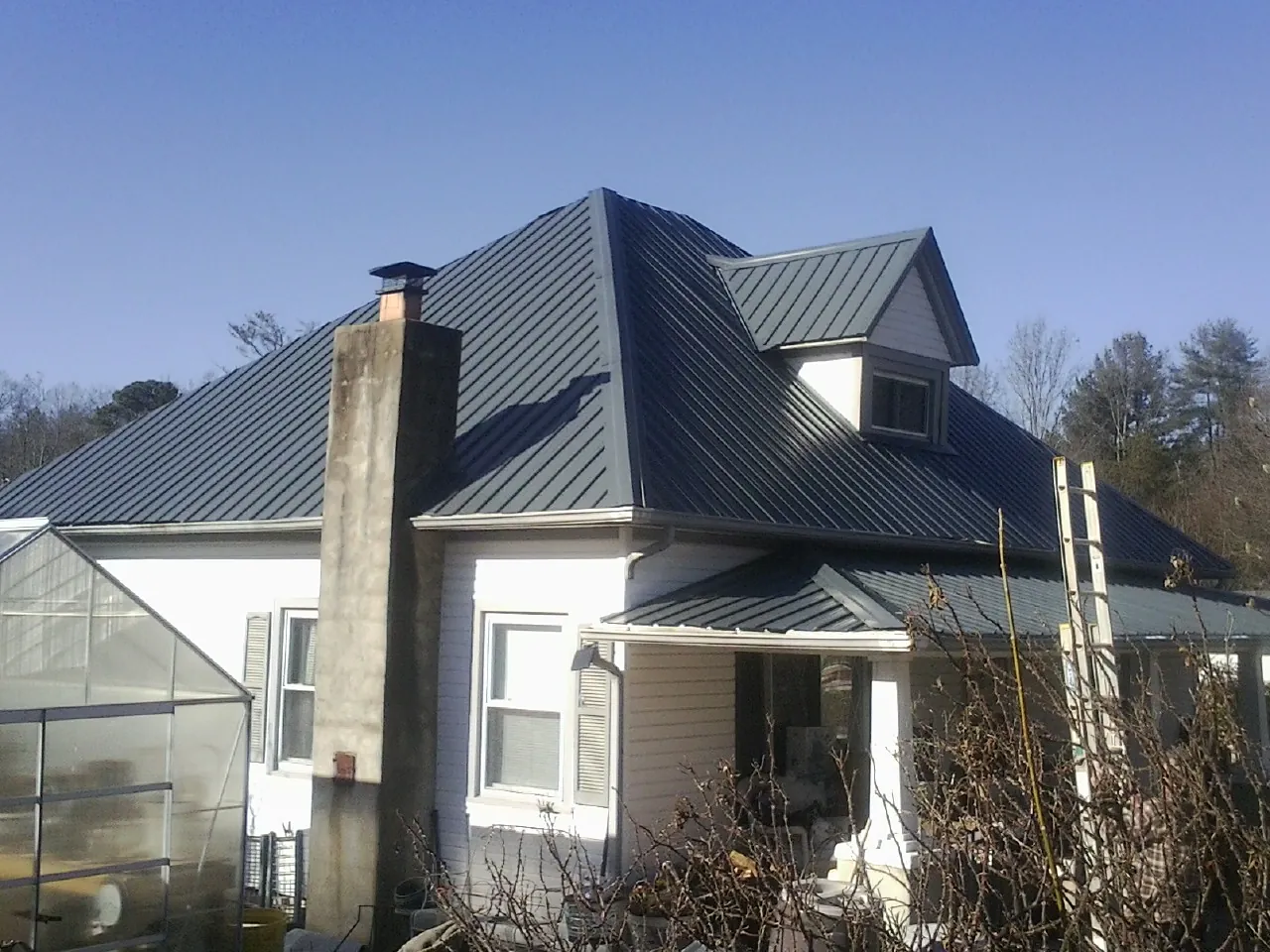 Dark blue standing seam metal roof on a white farmhouse with dormer — Slate & Tile Roof Repair by Roofing Brothers in Victorville