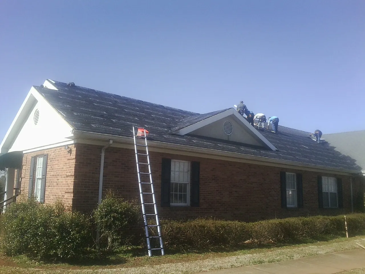Crew tearing shingles off a brick ranch roof with a ladder set — Emergency Roof Repair work by our crew in Victorville