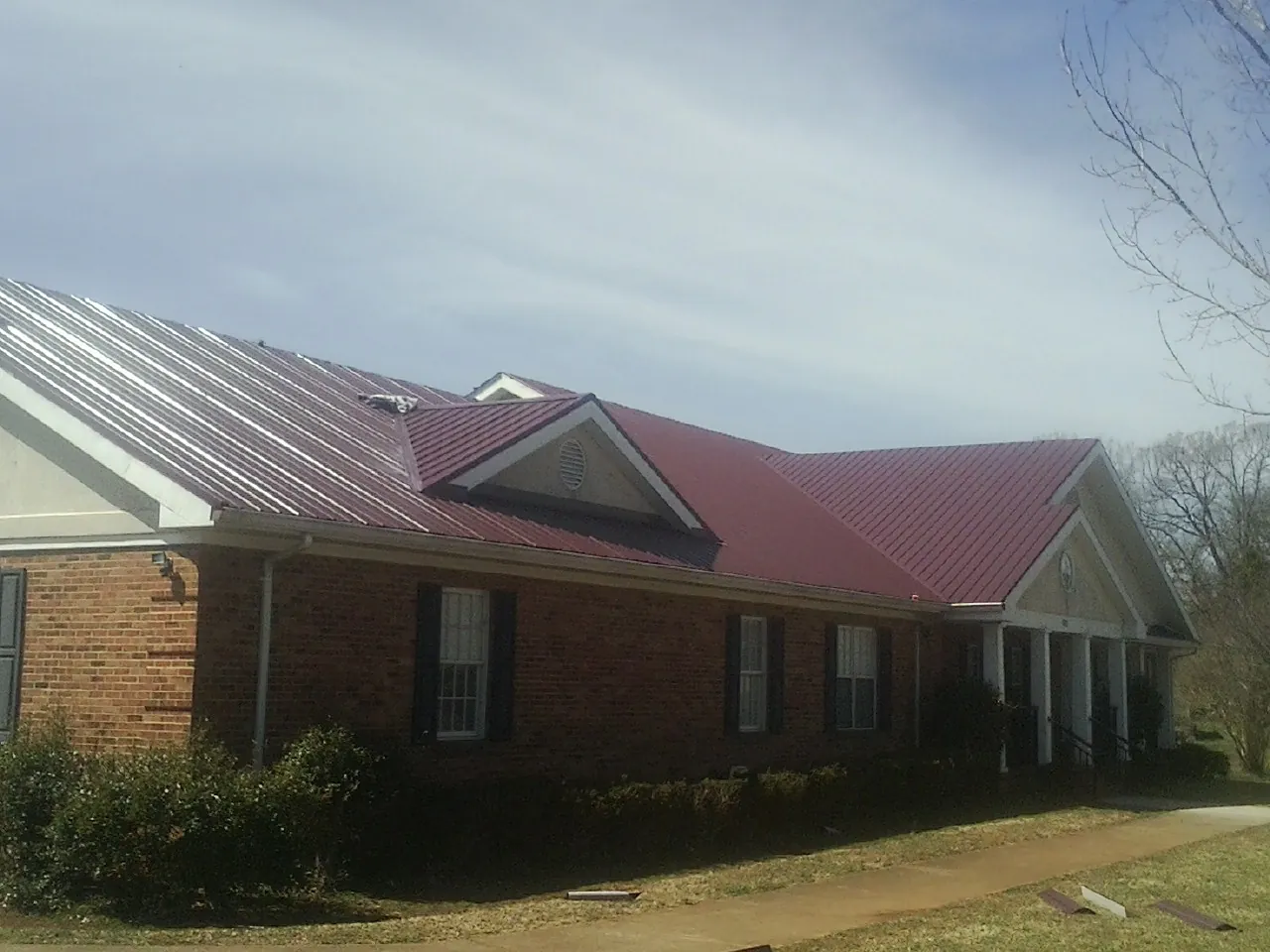 Red metal roof with gabled entries on a long brick building, from a Hail Damage Roof Repair job in Victorville