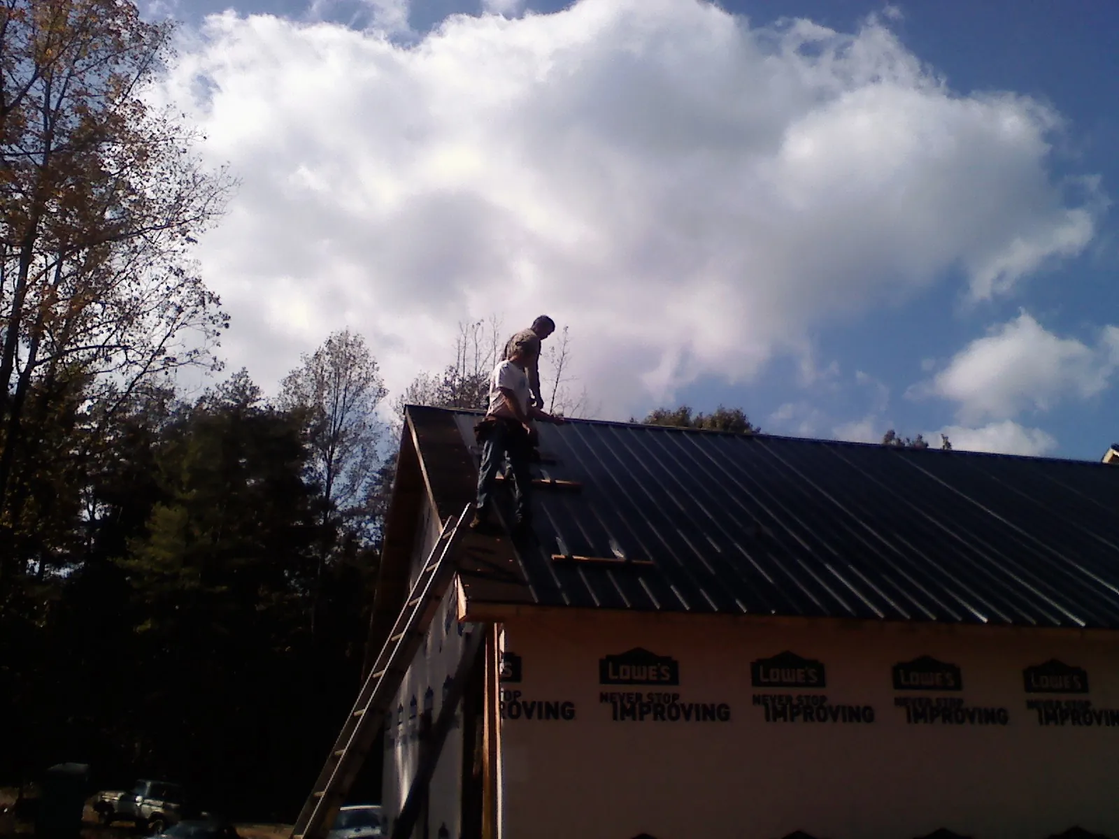 Roofer fastening dark metal panels high against a cloudy sky, from a Roof Inspection job in Victorville