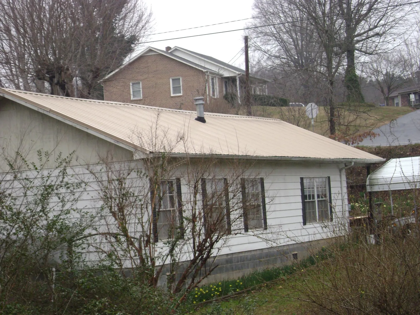 Tan metal roof on a white sided house set into a hillside — Commercial Roofing by Roofing Brothers in Victorville